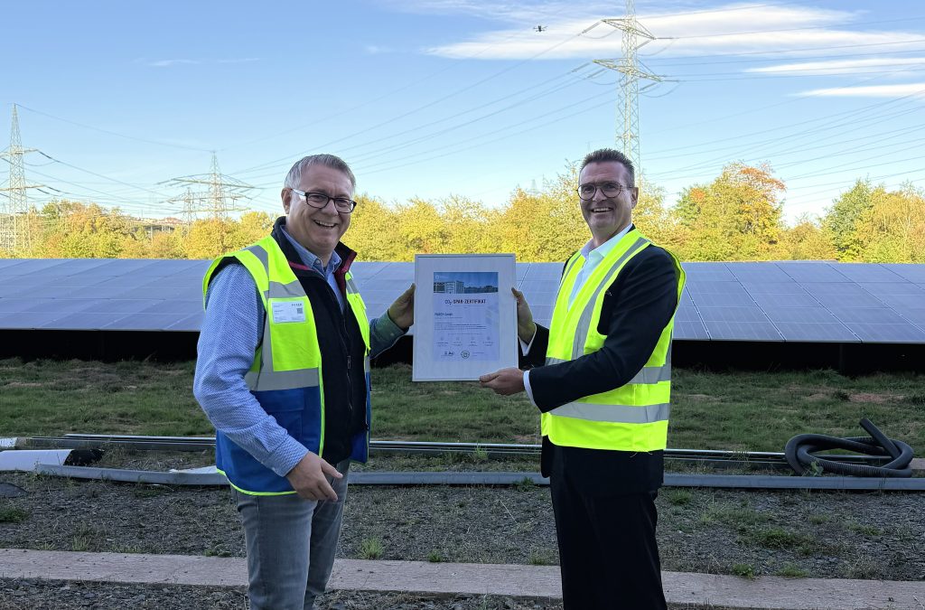 Übergabe des CO₂-Spar-Zertifikats vor einer Photovoltaikanlage mit zwei Personen in Warnwesten.